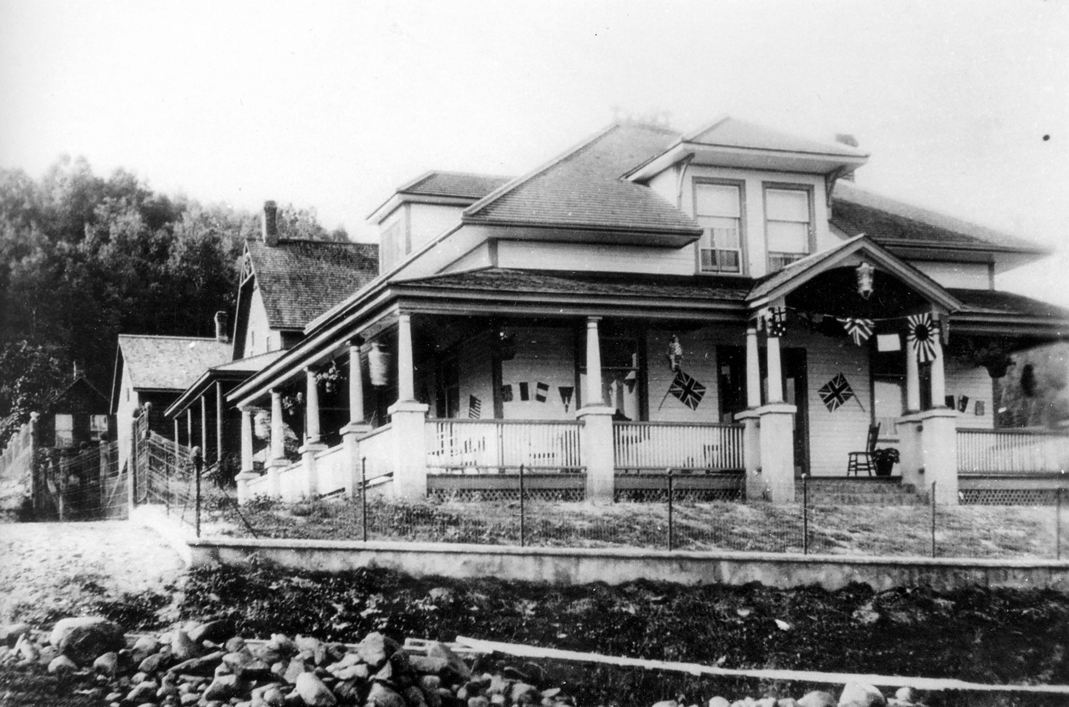 Old black and white photo taken of a historic home in Dysart. The home has peaked windows and a wrap around covered porch