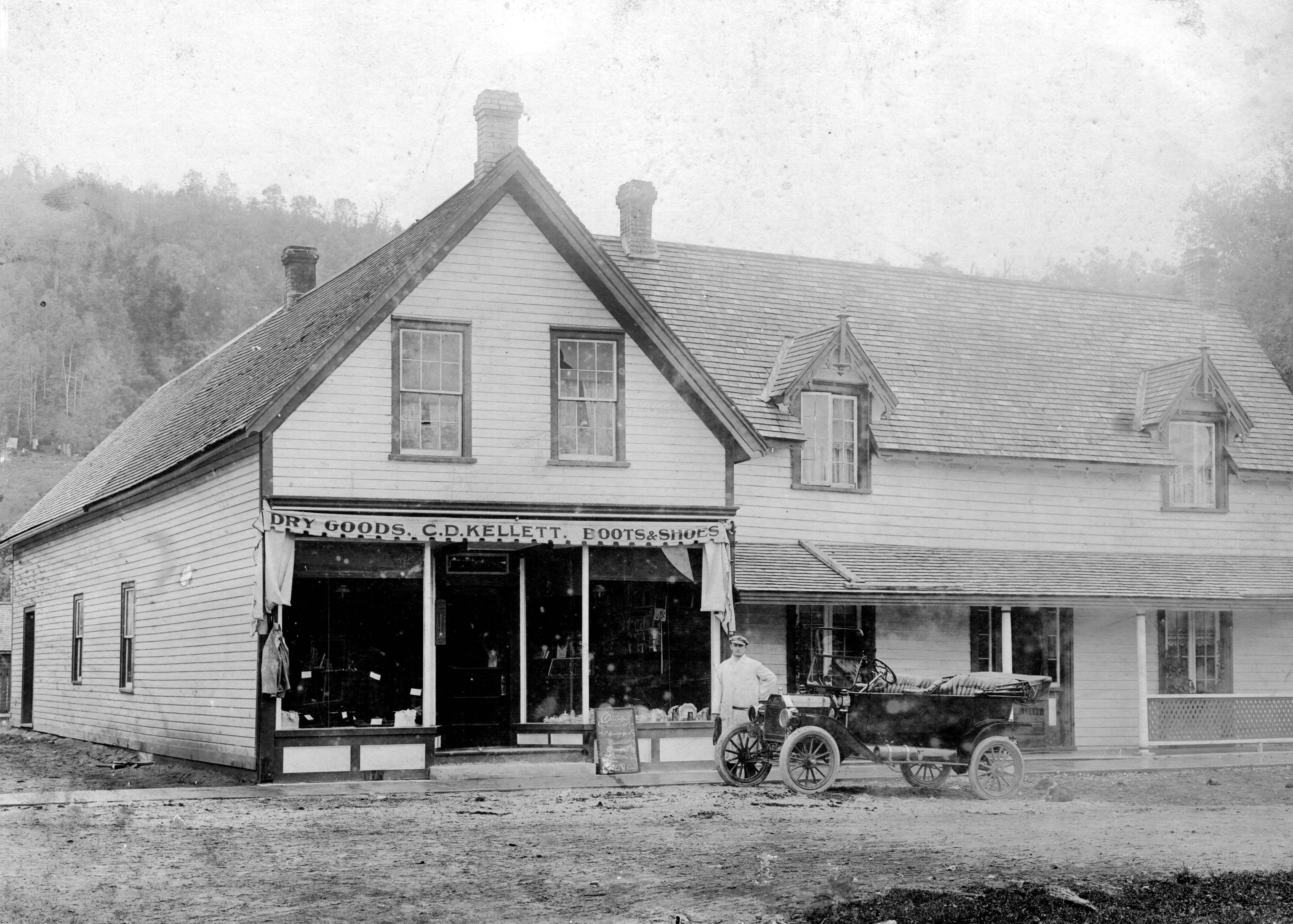 White wood sided building with a picture of a man in a white suite standing beside a Model-T Ford