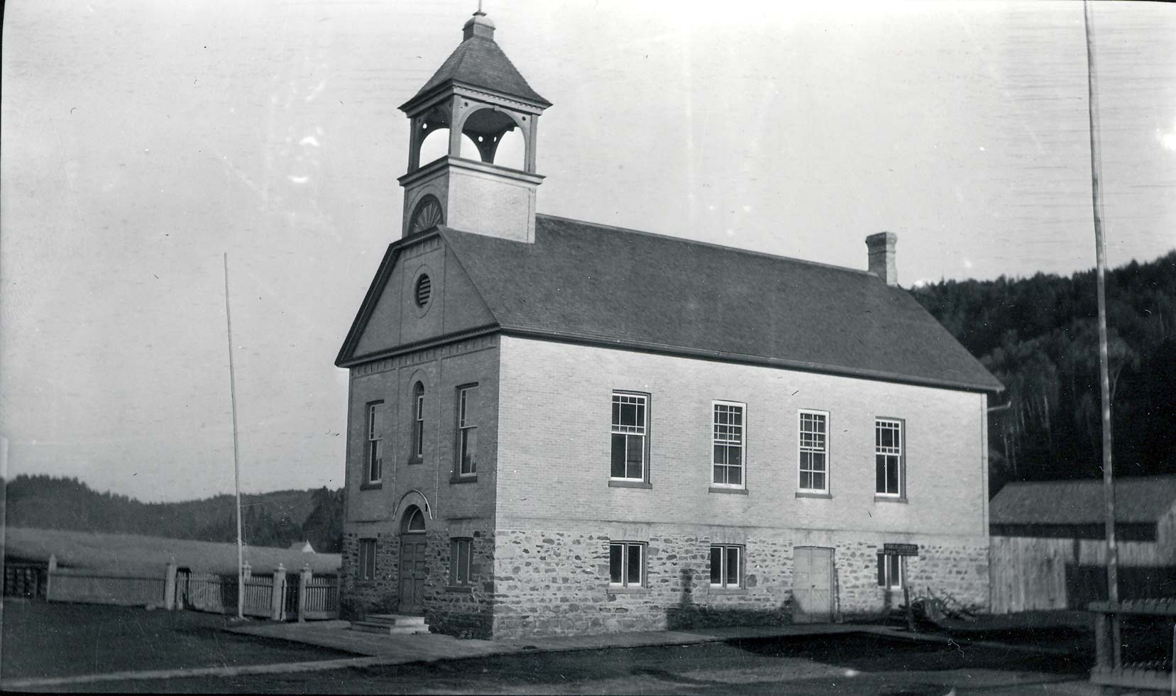 Large building with a bell tower on top, a stone foundation and brick exterior.