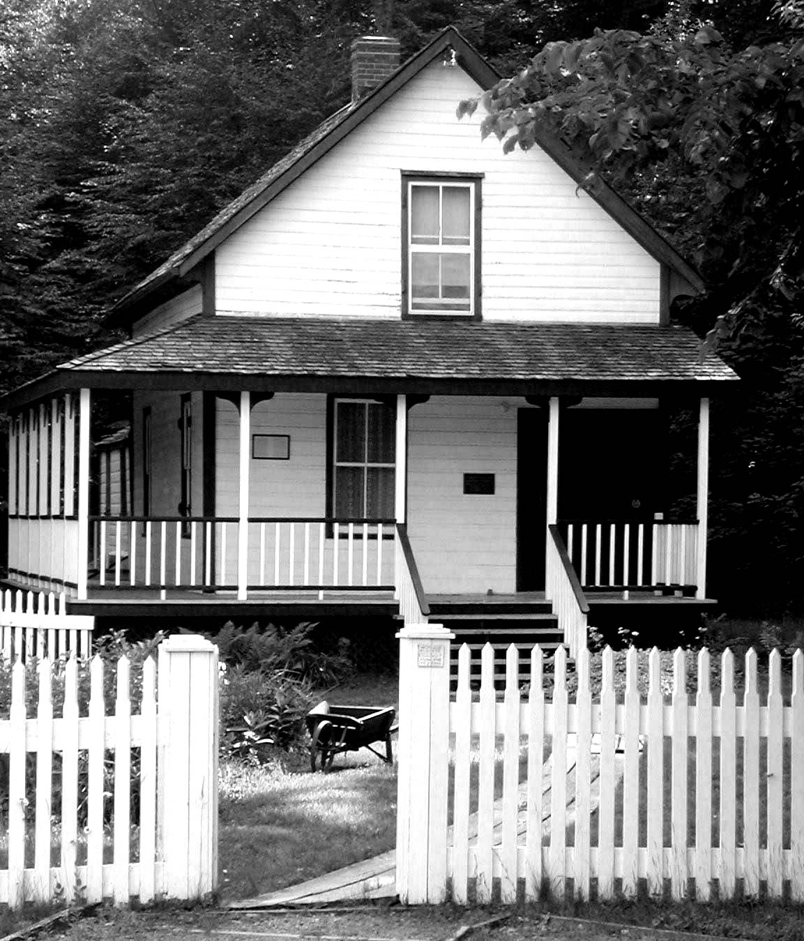 White two story home with a wrap around porch and white picket fence.