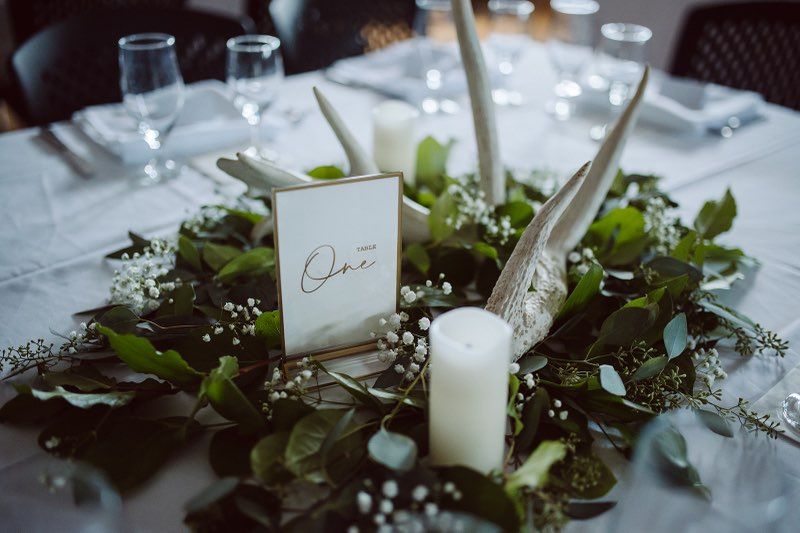 Centre piece with white candle, deer antlers and greenery.